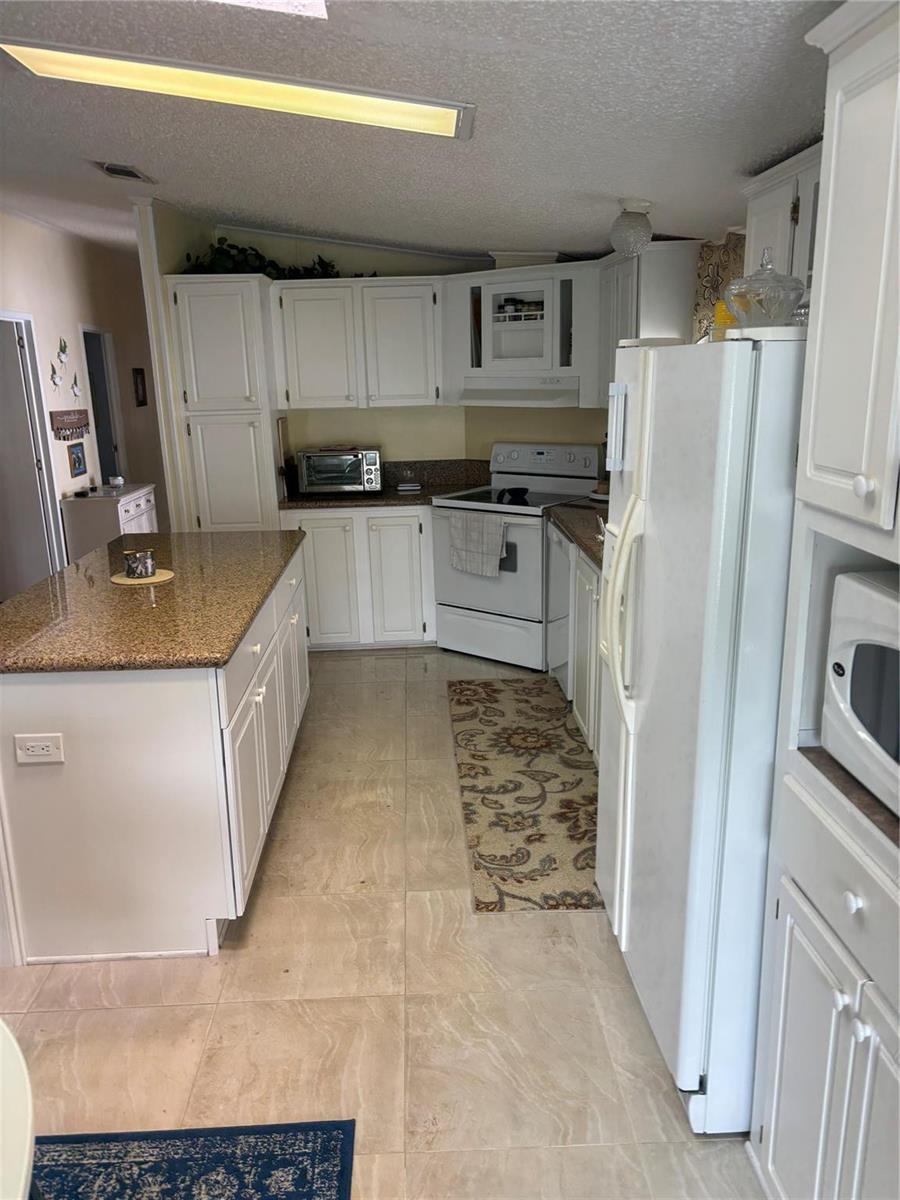A kitchen features white cabinets, granite countertops, a center island, and white appliances — 5116 NW 4th Avenue, Deerfield Beach FL 33064, DEERFIELD BEACH, FL