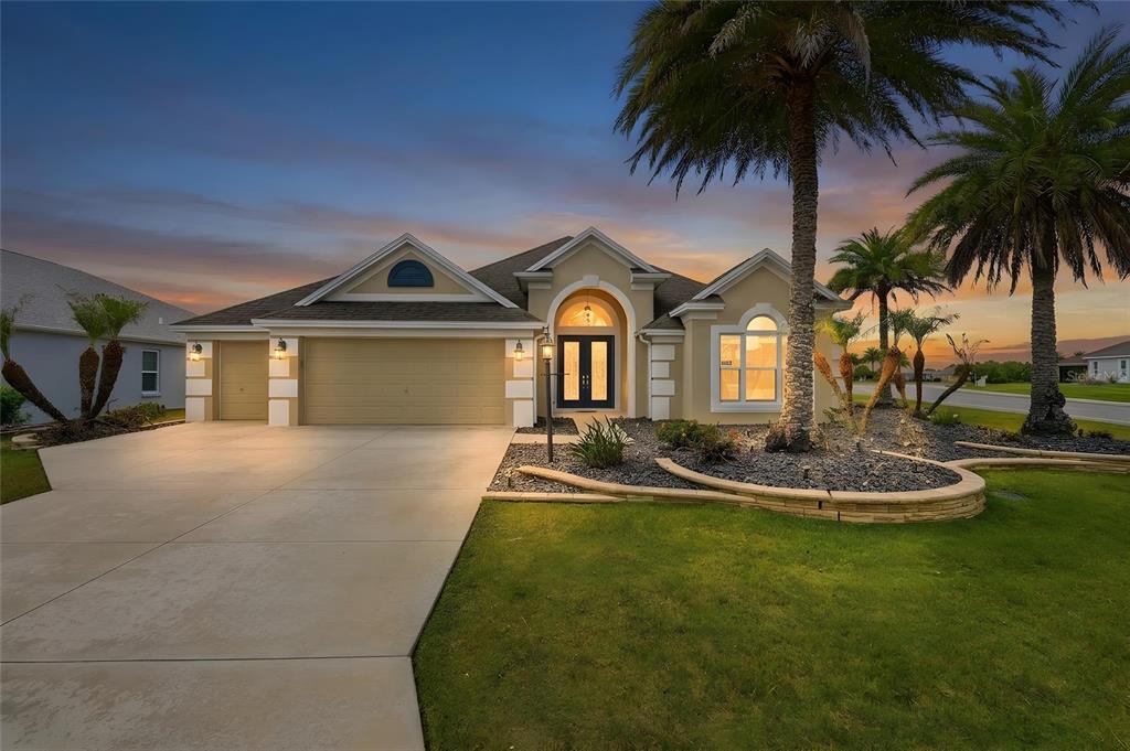 A single-story house with a beige exterior, a two-car garage, and palm trees at dusk — 1166 BLOUNT AVENUE, THE VILLAGES, FL