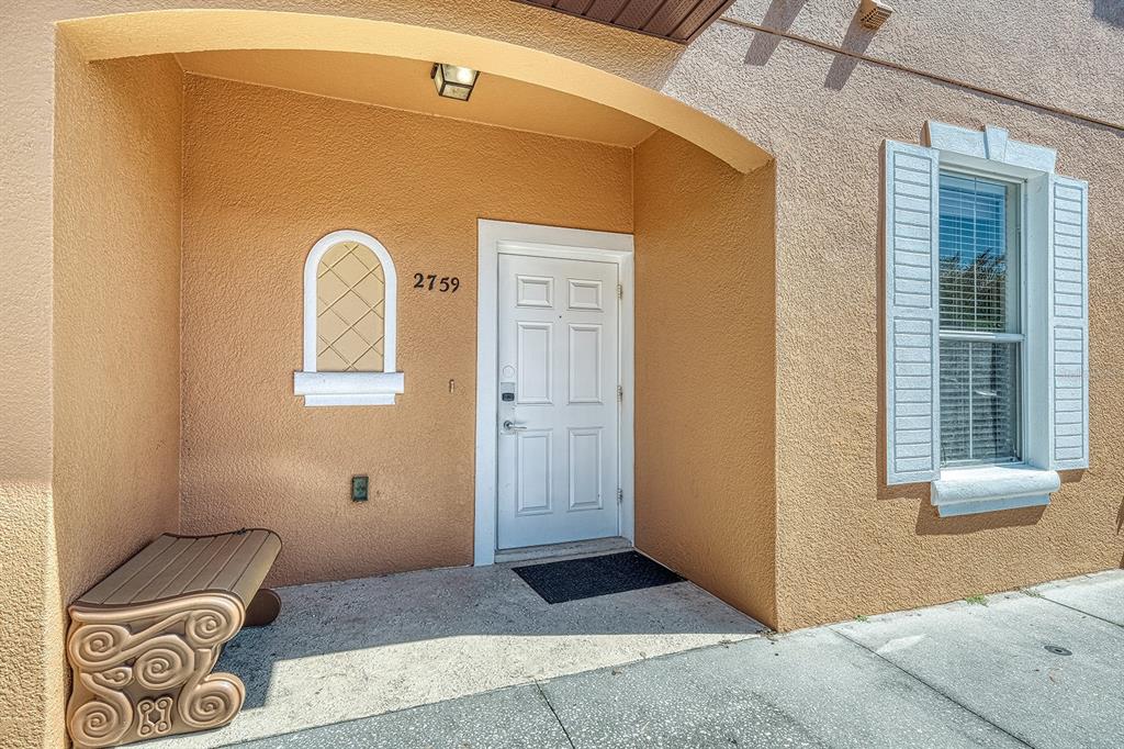 An exterior view of a home entrance featuring a white door, bench, and arched window — 2759 CORVETTE LANE, KISSIMMEE, FL