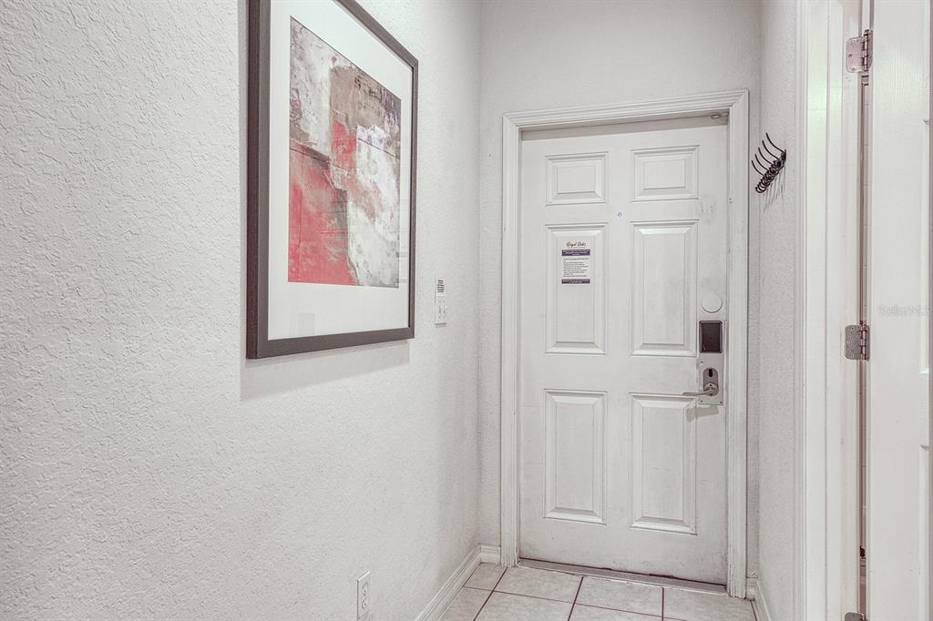 A white door with a digital lock stands in a tiled entryway with framed art — 2759 CORVETTE LANE, KISSIMMEE, FL