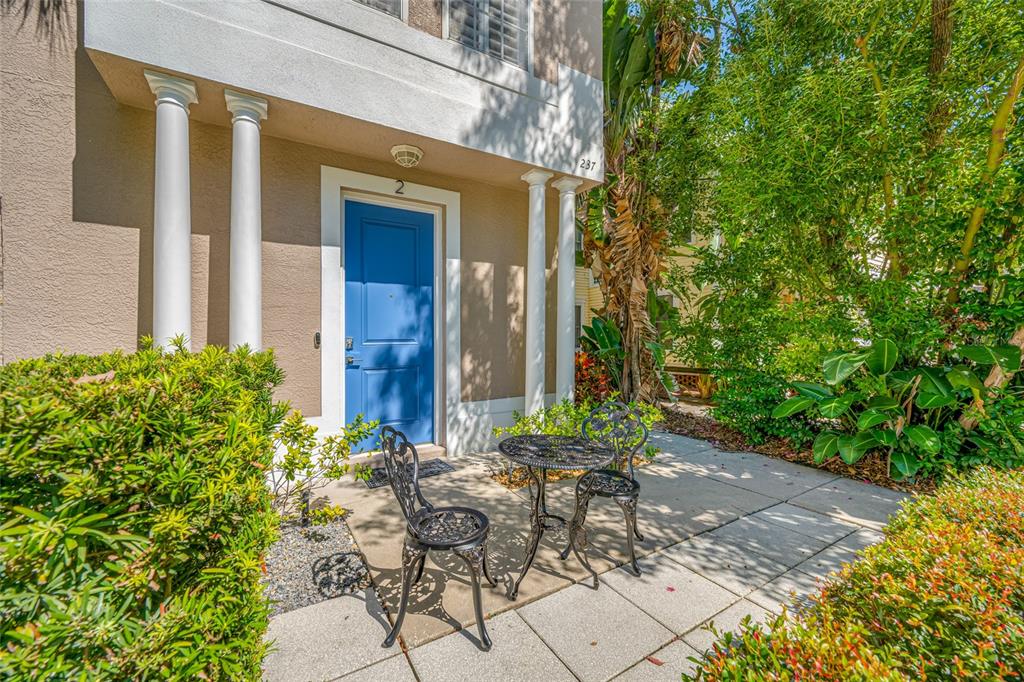 A small patio with a metal table and two chairs sits amidst lush green landscaping — 237 7TH AVENUE N UNIT 2, ST PETERSBURG, FL