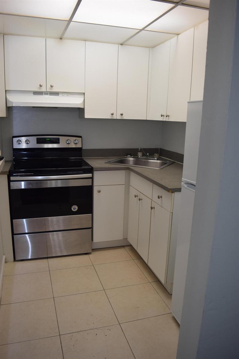 A small kitchen features white cabinets, stainless steel appliances, a corner sink, and tiled flooring — 151 SE 6th Avenue # 14, Pompano Beach FL 33060, POMPANO BEACH, FL