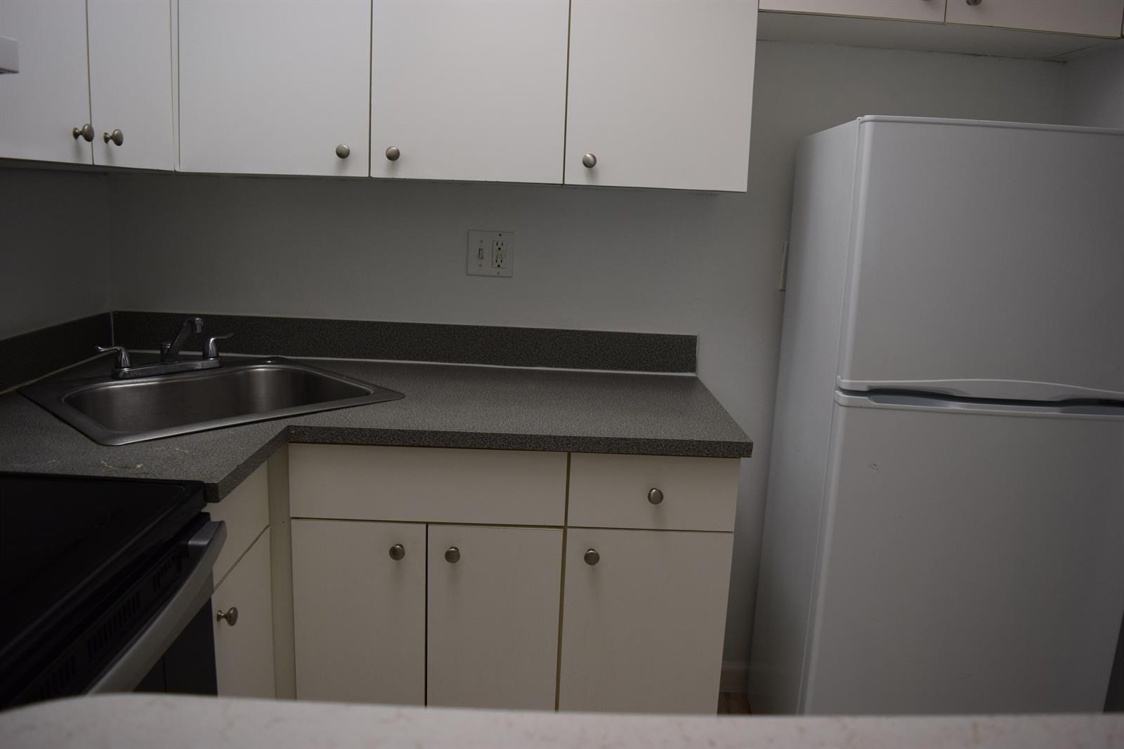 A kitchen features white cabinets, a stainless steel sink, gray countertops, and a white refrigerator — 151 SE 6th Avenue # 14, Pompano Beach FL 33060, POMPANO BEACH, FL