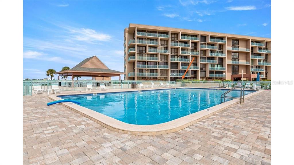 A swimming pool sits in front of a multi-story apartment building with a patio area — 1 KEY CAPRI UNIT 104-East, TREASURE ISLAND, FL