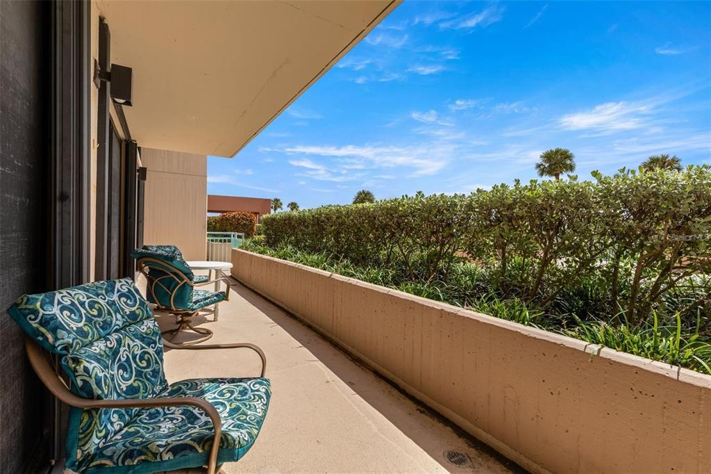 A balcony features two patterned chairs, a small table, and a low concrete wall — 1 KEY CAPRI UNIT 104-East, TREASURE ISLAND, FL