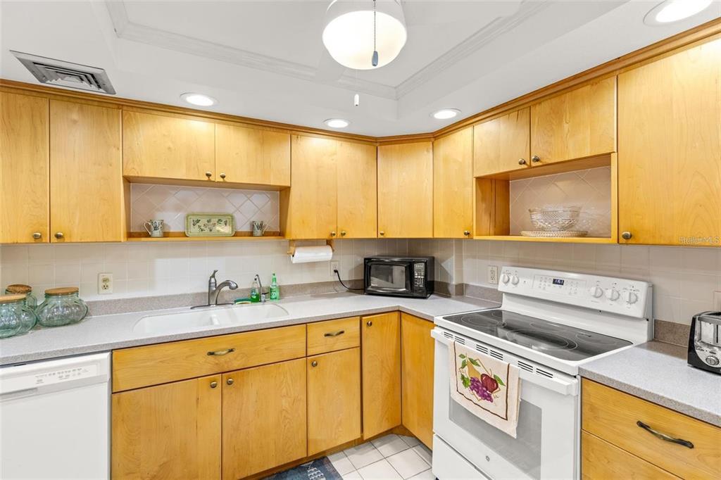A kitchen with light wood cabinets, white countertops, a white stove, and a double sink — 1 KEY CAPRI UNIT 104-East, TREASURE ISLAND, FL