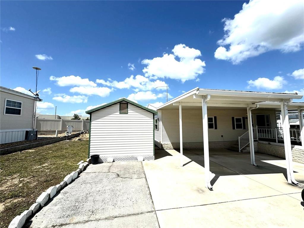 A white shed stands on a concrete driveway next to a mobile home carport — 917 ST GEORGE DRIVE, DAVENPORT, FL