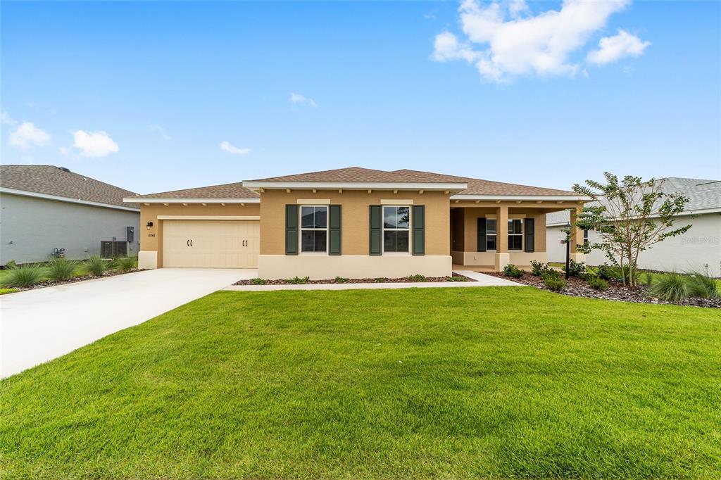 A single-story suburban house features a tan stucco exterior, a two-car garage, and green shutters — 10001 SW 106TH CIRCLE, OCALA, FL