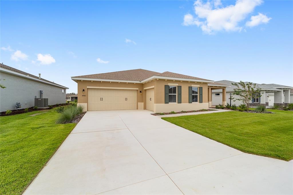 A tan single-story house with a three-car garage and a concrete driveway under a blue sky — 10001 SW 106TH CIRCLE, OCALA, FL