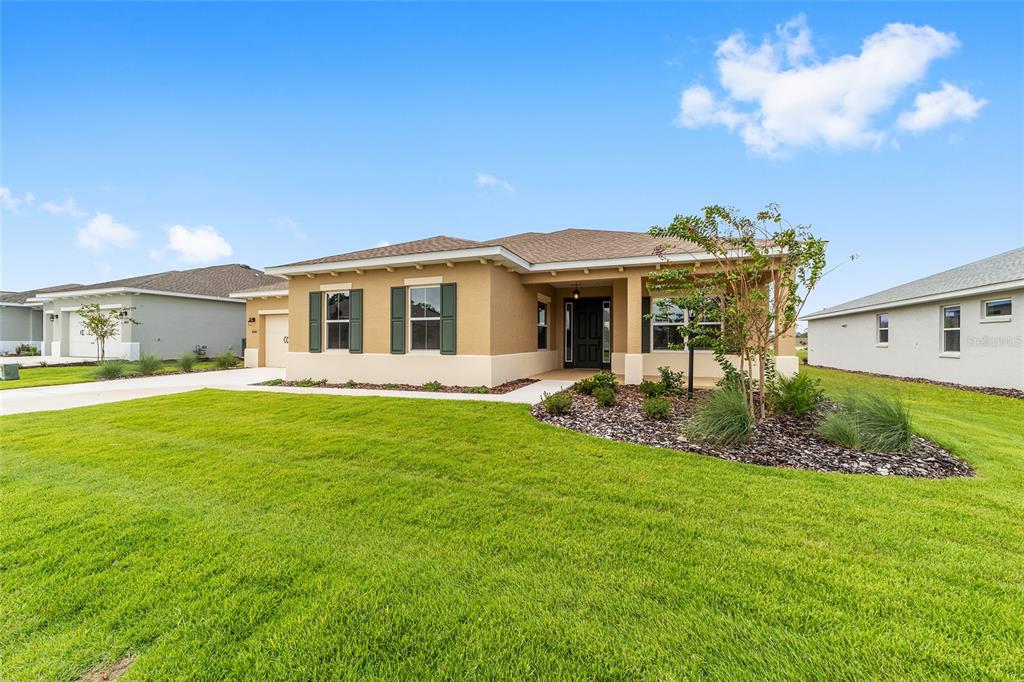 A tan single-story house with green shutters, a covered entryway, and a landscaped front yard — 10001 SW 106TH CIRCLE, OCALA, FL