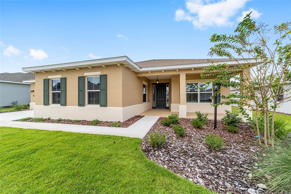 A single-story house with tan stucco walls, green shutters, and a covered front porch — 10001 SW 106TH CIRCLE, OCALA, FL