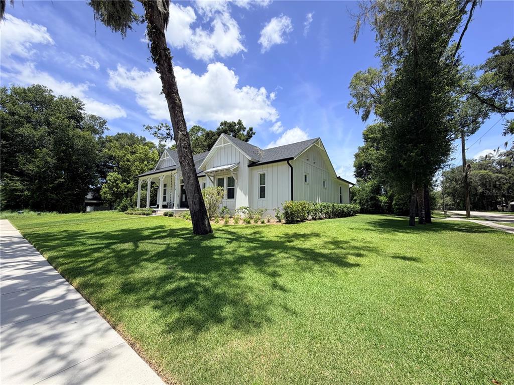 A white farmhouse-style home with a dark roof sits on a large, grassy lot — 310 W WASHINGTON AVENUE, LAKE HELEN, FL