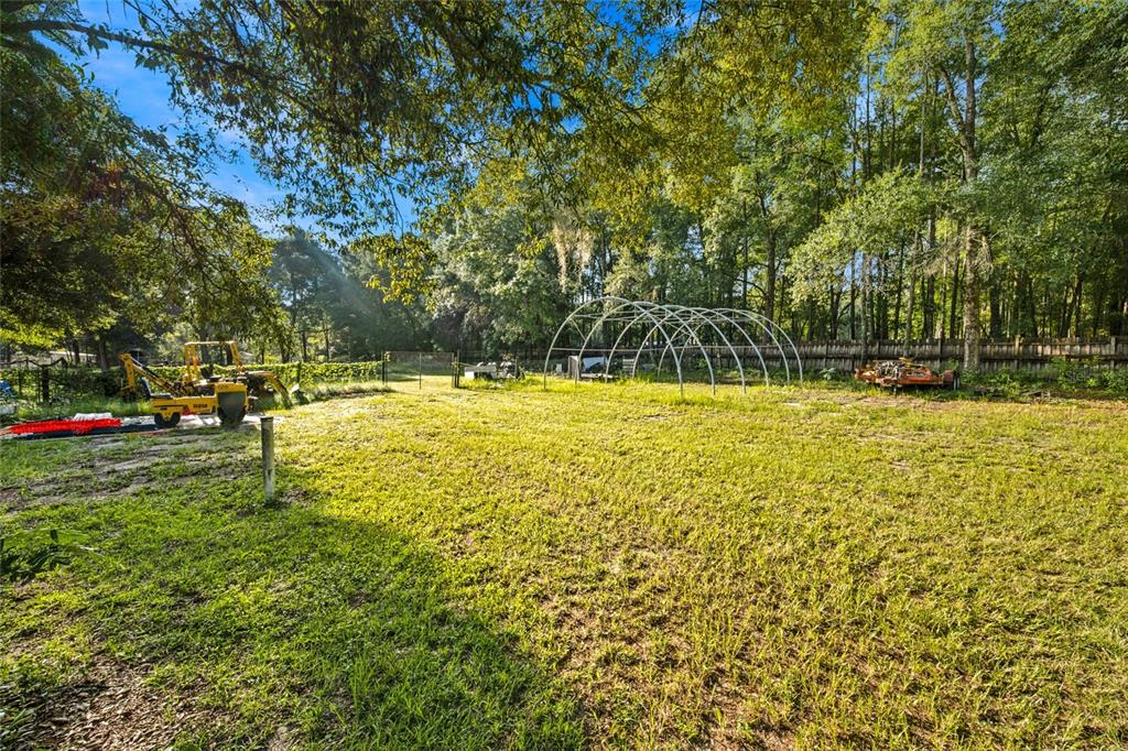 A grassy backyard features a metal greenhouse frame, a yellow tractor, and surrounding trees — 3025 S US HIGHWAY 41, DUNNELLON, FL
