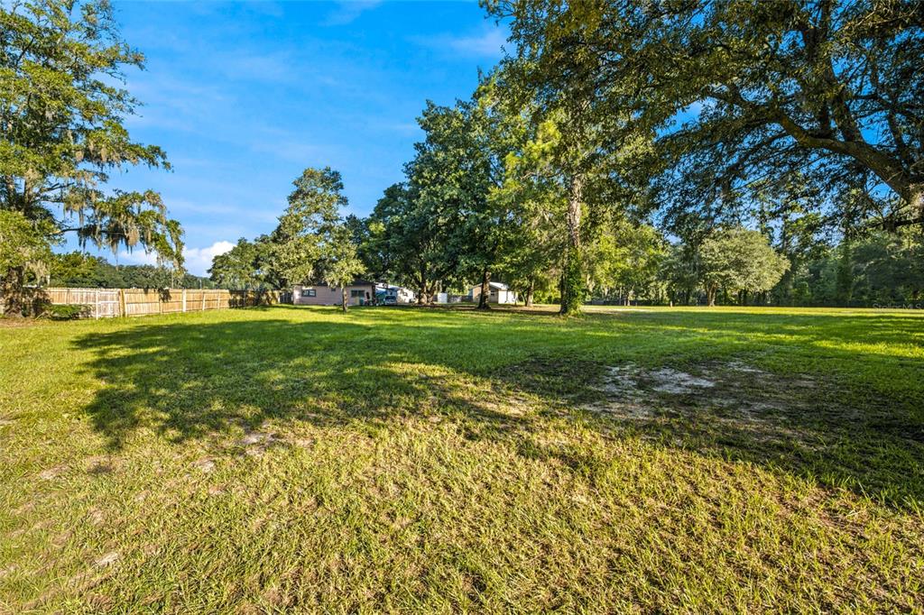 A large, grassy backyard features mature trees and a wooden fence under a blue sky — 3025 S US HIGHWAY 41, DUNNELLON, FL