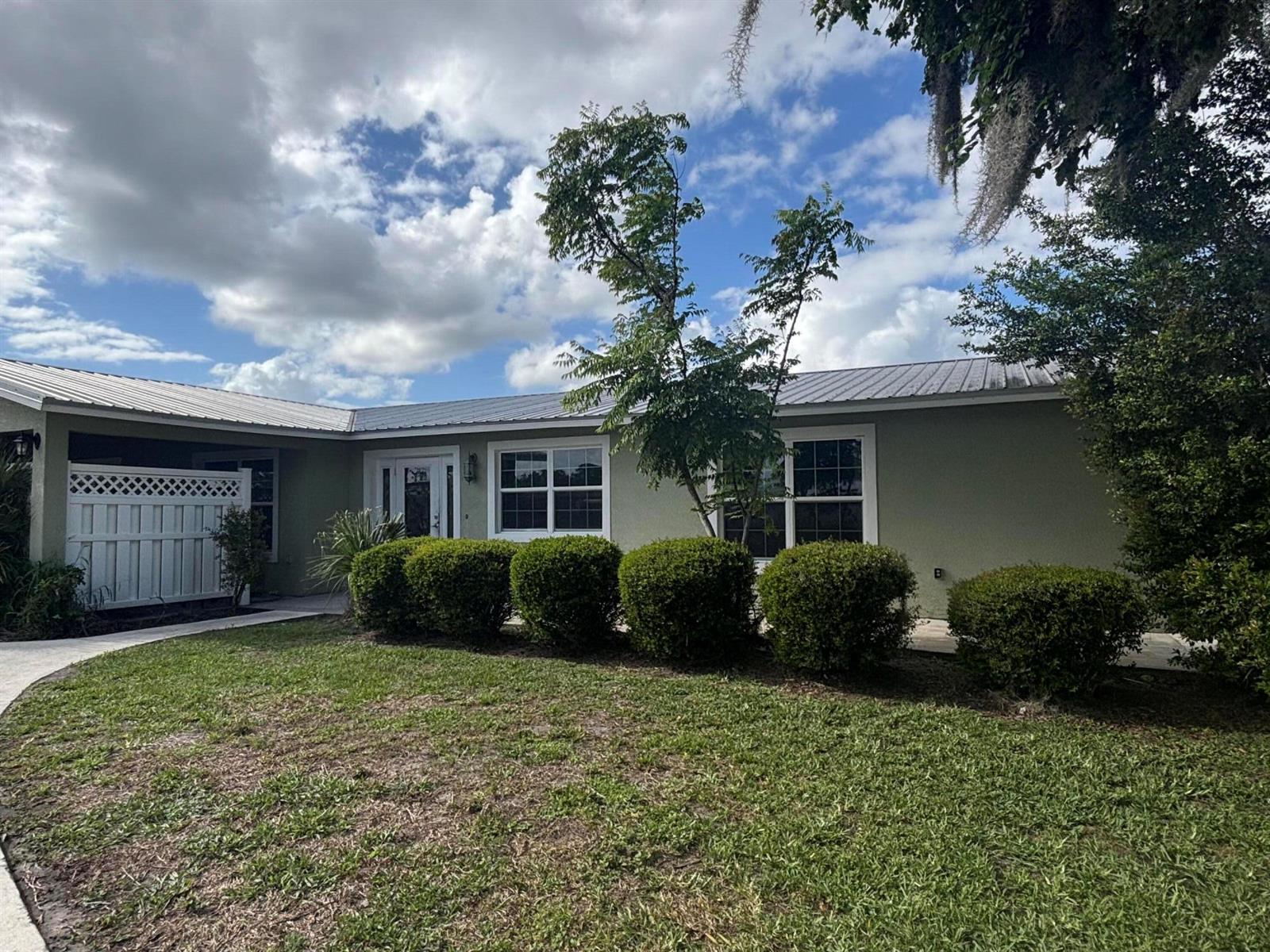 A single-story house with a green exterior, metal roof, and a row of manicured shrubs — 4003 SE 26th Street, Okeechobee FL 34974, OKEECHOBEE, FL
