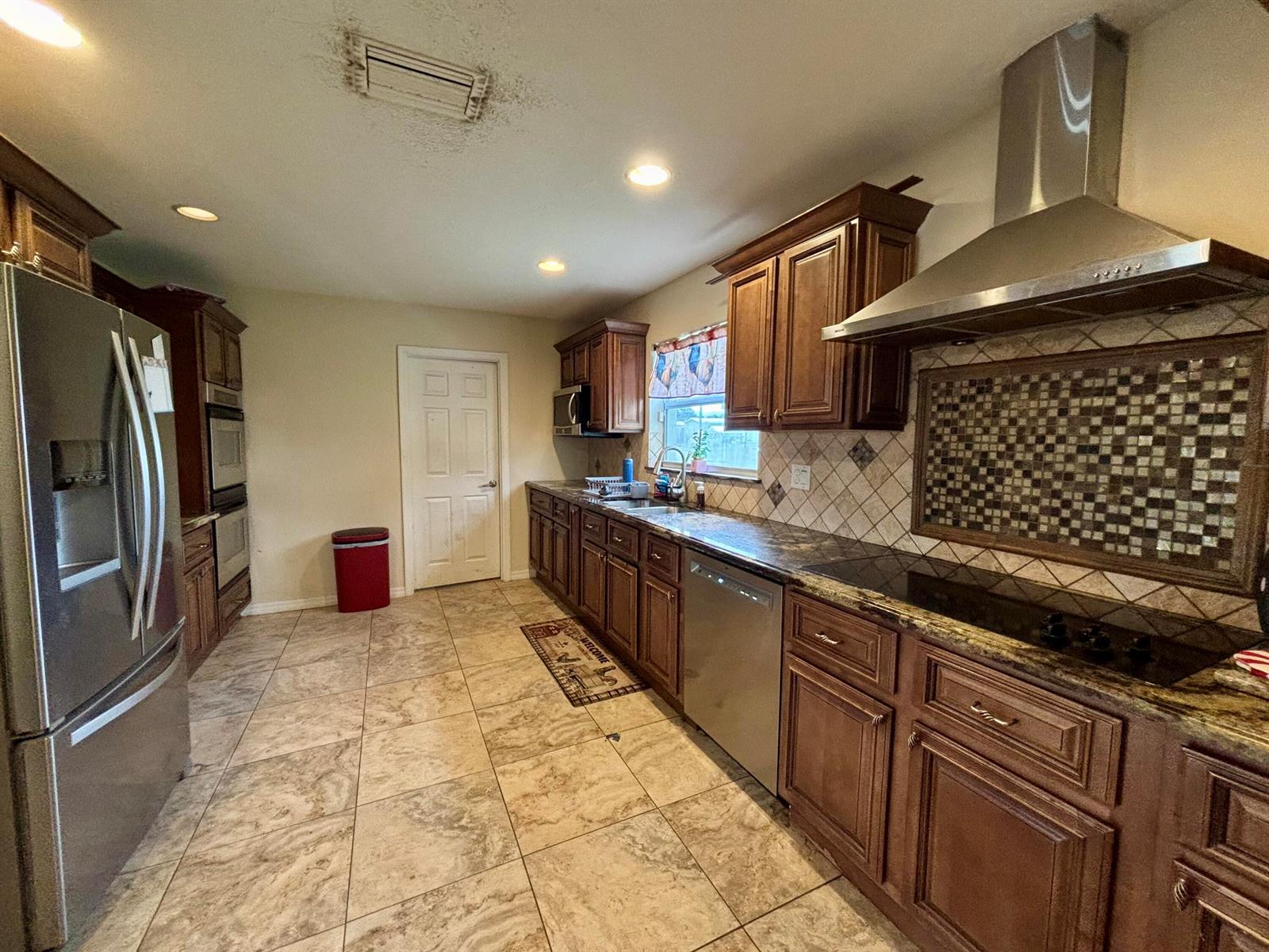 A kitchen features dark wood cabinets, stainless steel appliances, tile flooring, and a mosaic backsplash — 4003 SE 26th Street, Okeechobee FL 34974, OKEECHOBEE, FL