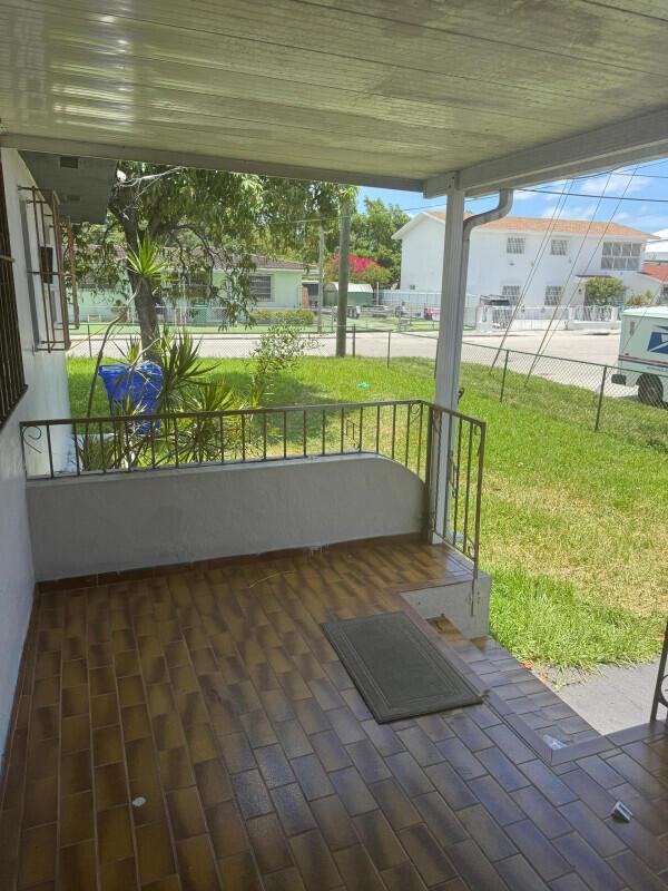 A covered porch with brown tiled flooring, a metal railing, and a view of the yard — 88 NW 18th Avenue, Miami FL 33125, MIAMI, FL