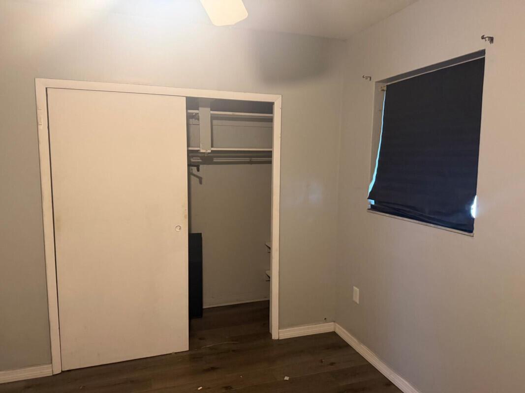 A bedroom with light gray walls, wood-look flooring, a sliding closet door, and a window — 88 NW 18th Avenue, Miami FL 33125, MIAMI, FL