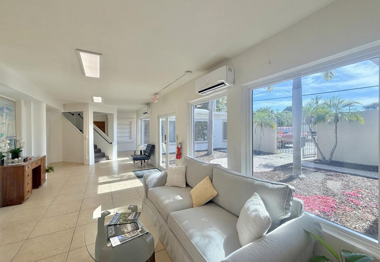 A bright lobby features a grey sofa, tile flooring, and large windows overlooking a courtyard — 3600 Broadway, West Palm Beach FL 33407, WEST PALM BEACH, FL