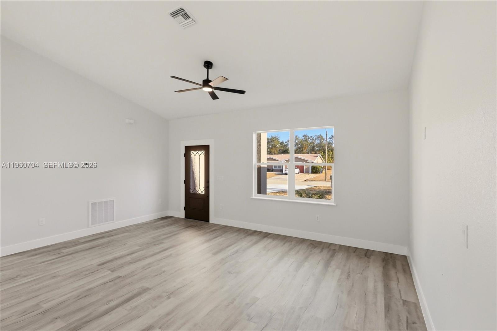 An empty room features light wood-look flooring, white walls, a ceiling fan, and a door — 3825 Citroen Dr, Sebring FL 33872, SEBRING, FL