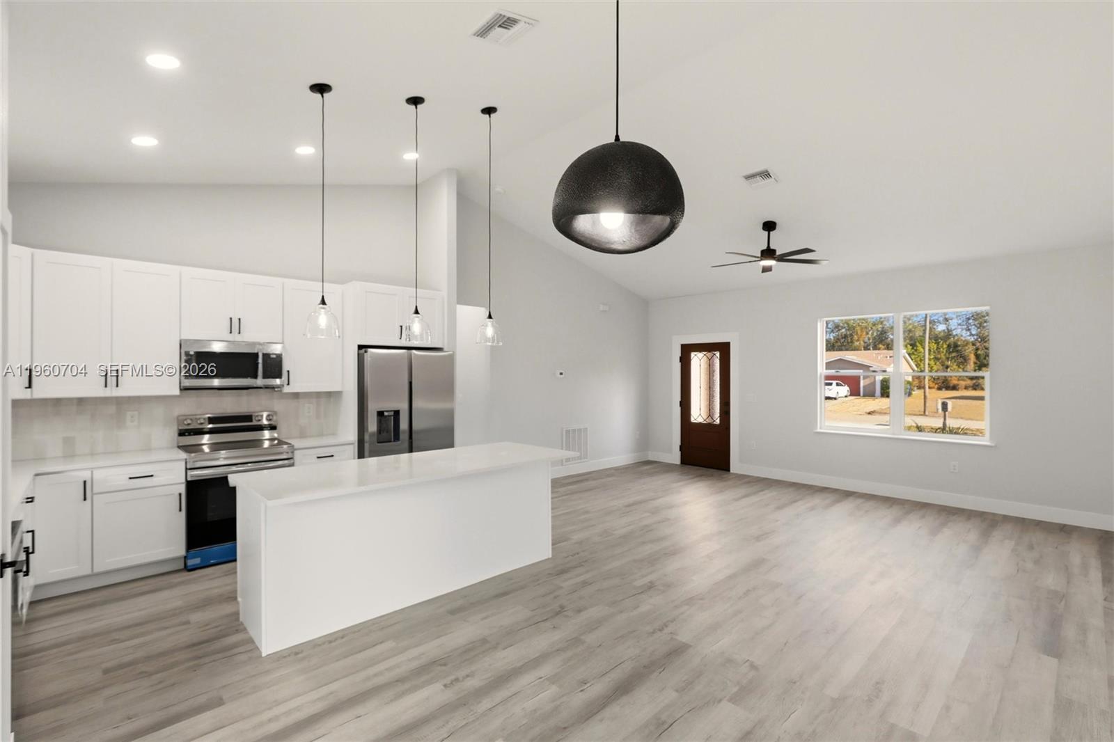 A modern kitchen with white cabinets and an island opens into a spacious living area — 3825 Citroen Dr, Sebring FL 33872, SEBRING, FL