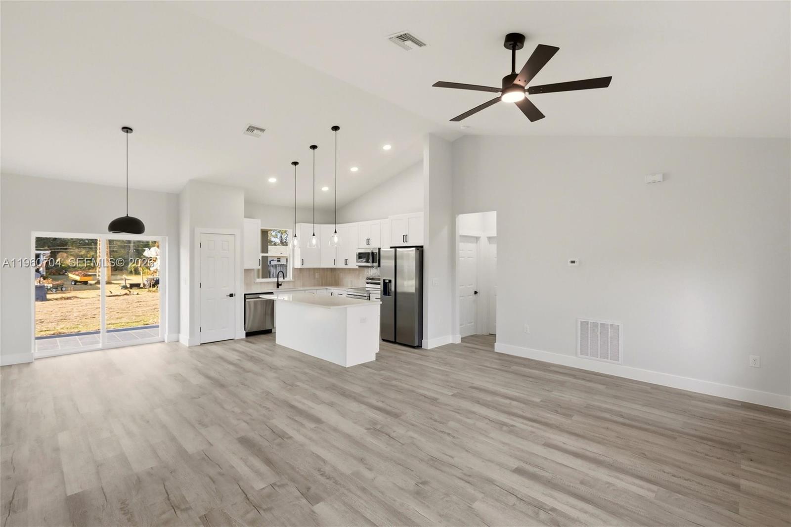 A modern open-concept kitchen and living area features white cabinetry, stainless appliances, and wood-look flooring — 3825 Citroen Dr, Sebring FL 33872, SEBRING, FL