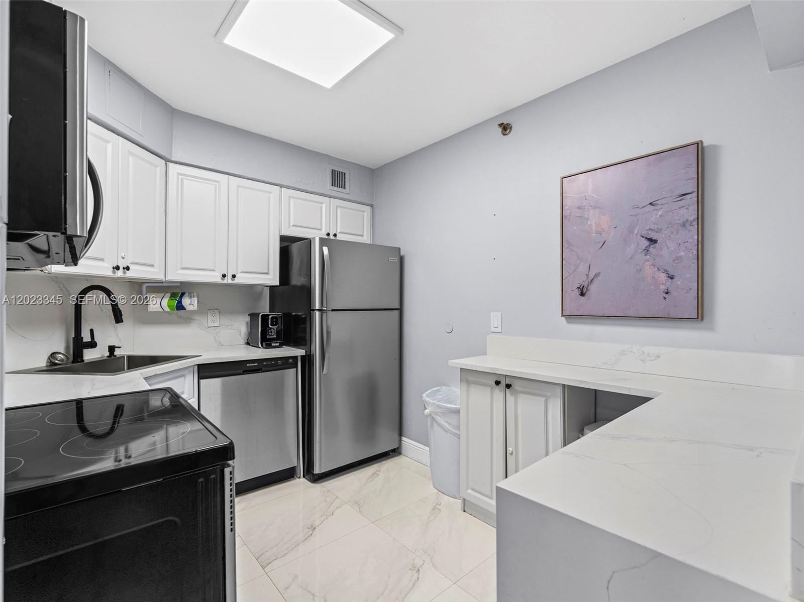 A kitchen features white cabinets, stainless steel appliances, and white marble-patterned countertops and flooring — 5225 Collins Ave # 1509, Miami Beach FL 33140, MIAMI BEACH, FL