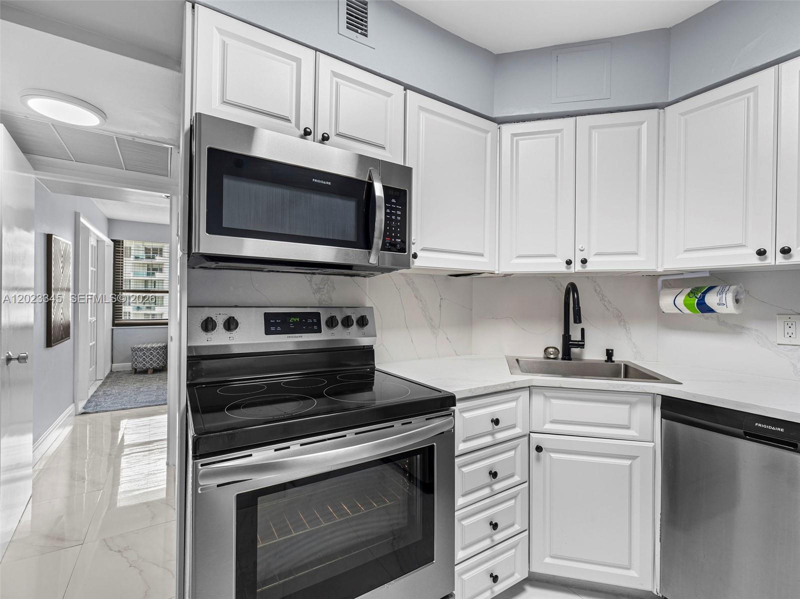A kitchen features white cabinets, stainless steel appliances, and a marble-patterned backsplash — 5225 Collins Ave # 1509, Miami Beach FL 33140, MIAMI BEACH, FL