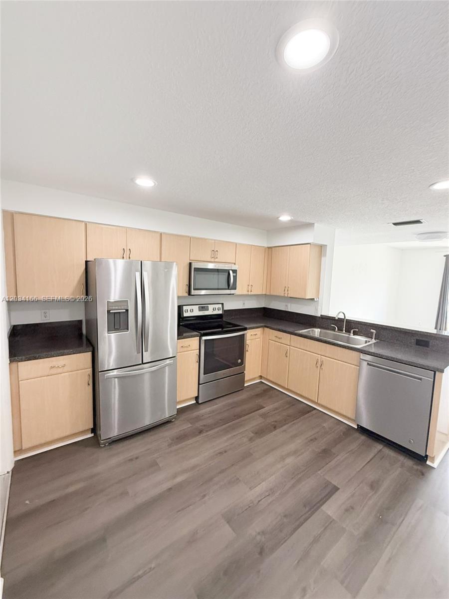 A kitchen features light wood cabinets, stainless steel appliances, and dark countertops over wood flooring — 1564 Veracruz Ln # 1564, Weston FL 33327, WESTON, FL