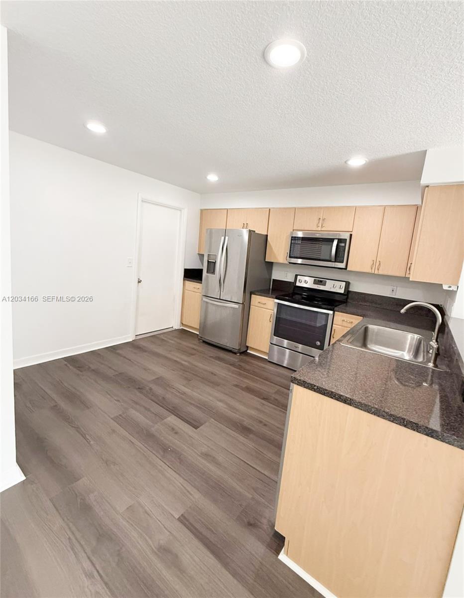 A kitchen features light wood cabinets, stainless steel appliances, and dark countertops over wood flooring — 1564 Veracruz Ln # 1564, Weston FL 33327, WESTON, FL