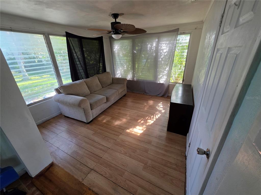 A sunroom with wood-look flooring, a beige sofa, and large windows with curtains — 563 MARTHA DRIVE, HOLLY HILL, FL