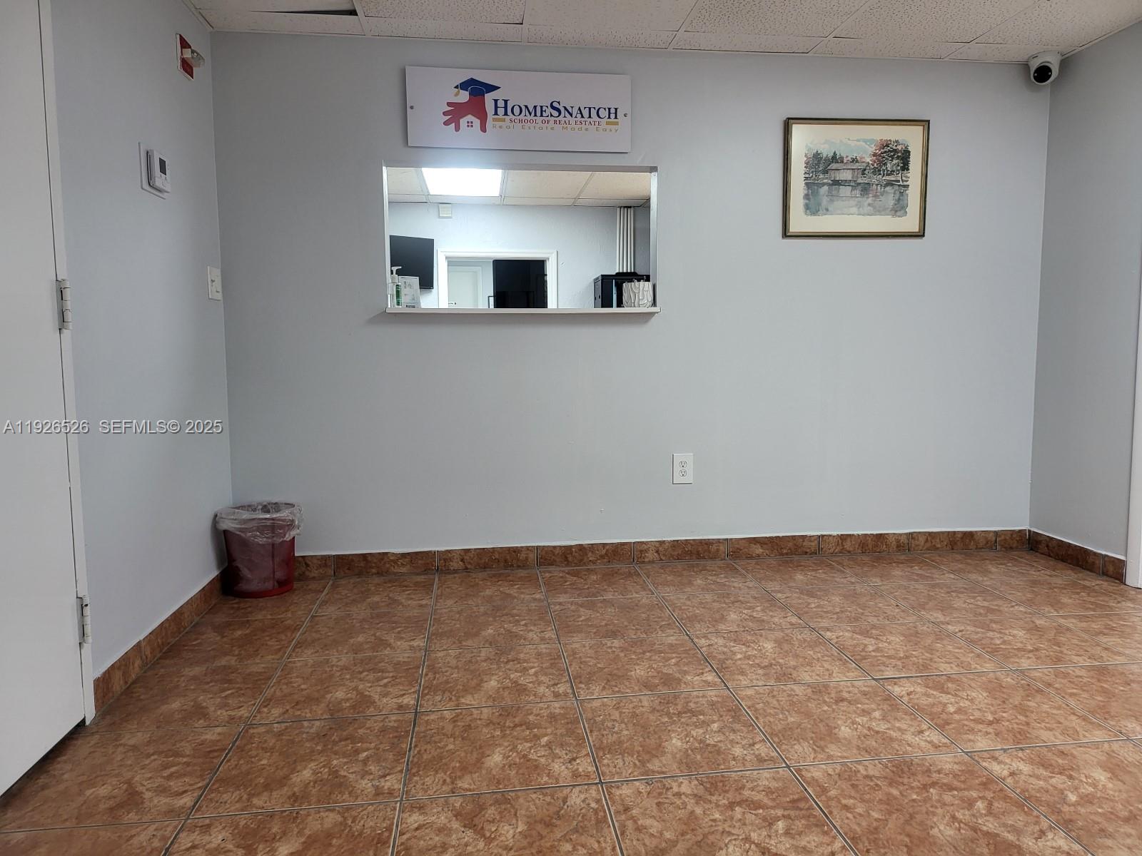 A room with light gray walls, brown tile flooring, and a service window with signage — 13499 Biscayne Blvd, North Miami FL 33181, NORTH MIAMI, FL