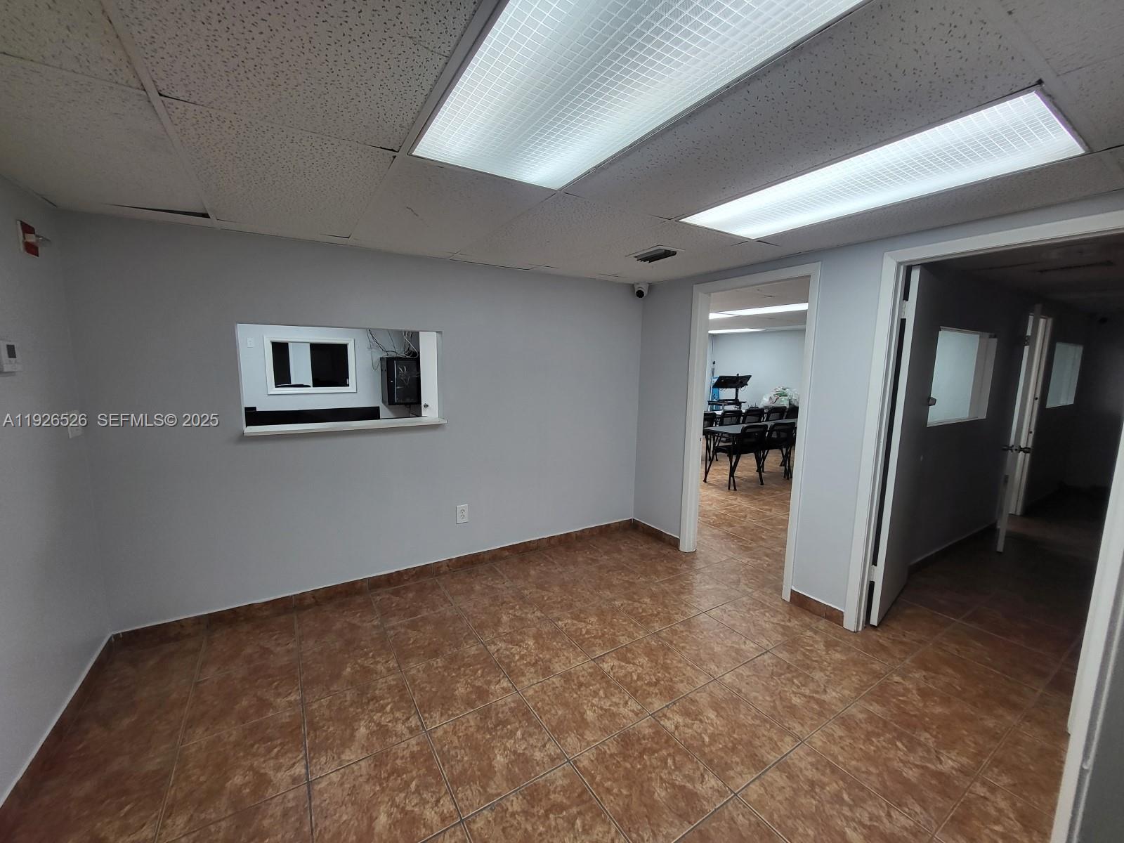 An office space features gray walls, brown tile flooring, and a rectangular interior service window — 13499 Biscayne Blvd, North Miami FL 33181, NORTH MIAMI, FL