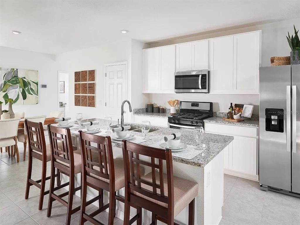 A kitchen features white cabinets, granite countertops, stainless steel appliances, and a breakfast bar island — 4909 KAIA AVENUE, WINTER HAVEN, FL