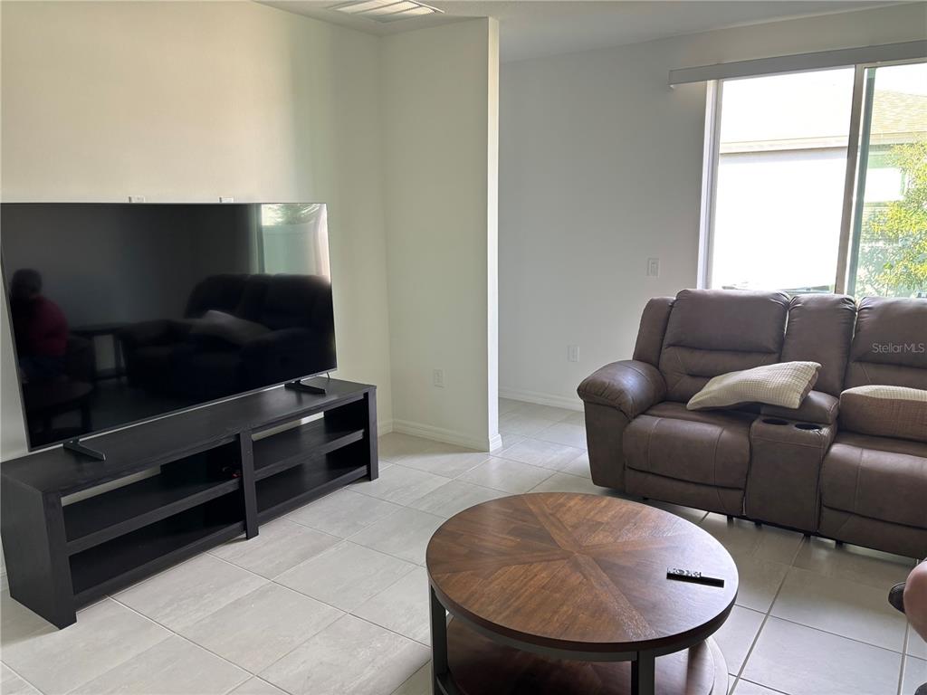 A living room features a large television on a black stand, a brown sofa, and tile flooring — 4909 KAIA AVENUE, WINTER HAVEN, FL