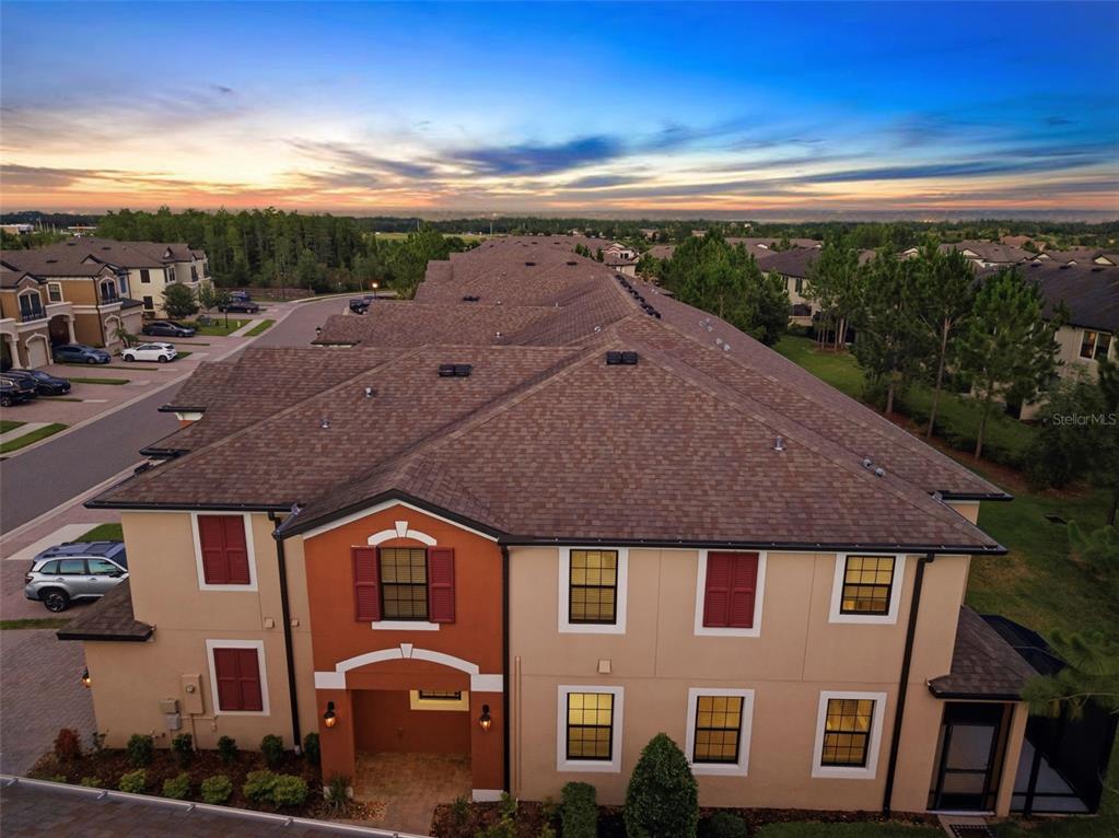 An aerial view of a multi-unit townhouse building with a brown shingled roof at sunset — 30040 SOUTHWELL LANE, WESLEY CHAPEL, FL