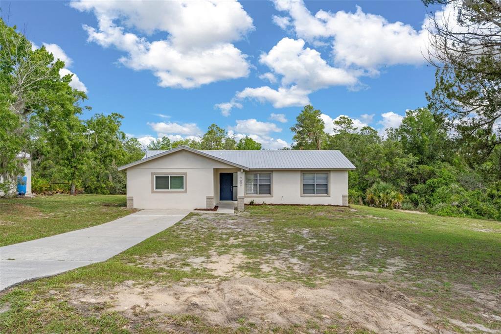 A single-story house with a metal roof, beige siding, and a concrete driveway — 7335 BLACKBIRD AVENUE, WEEKI WACHEE, FL