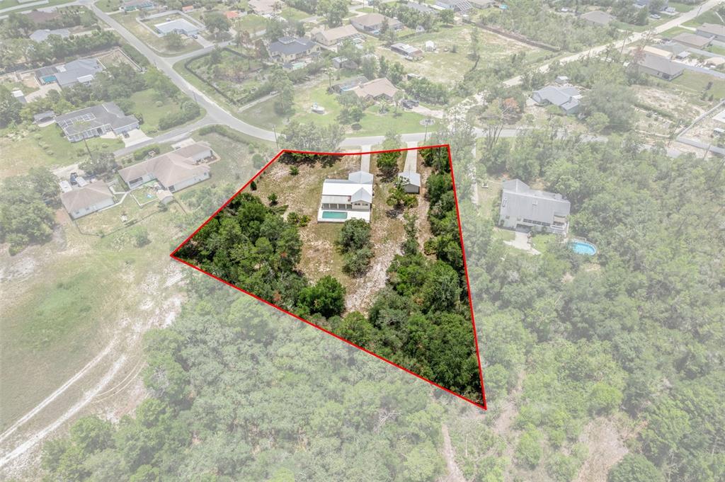 An aerial view shows a house with a pool on a large, wooded lot — 7335 BLACKBIRD AVENUE, WEEKI WACHEE, FL