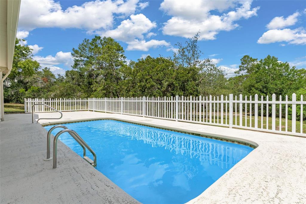 A rectangular swimming pool sits on a concrete patio enclosed by a white picket fence — 7335 BLACKBIRD AVENUE, WEEKI WACHEE, FL