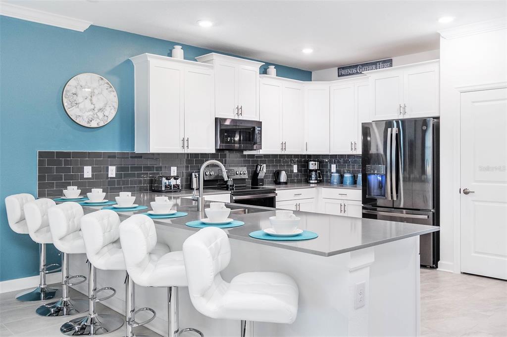 A kitchen features white cabinets, a gray island with bar stools, and a blue wall — 2766 OXYMORON WAY, KISSIMMEE, FL