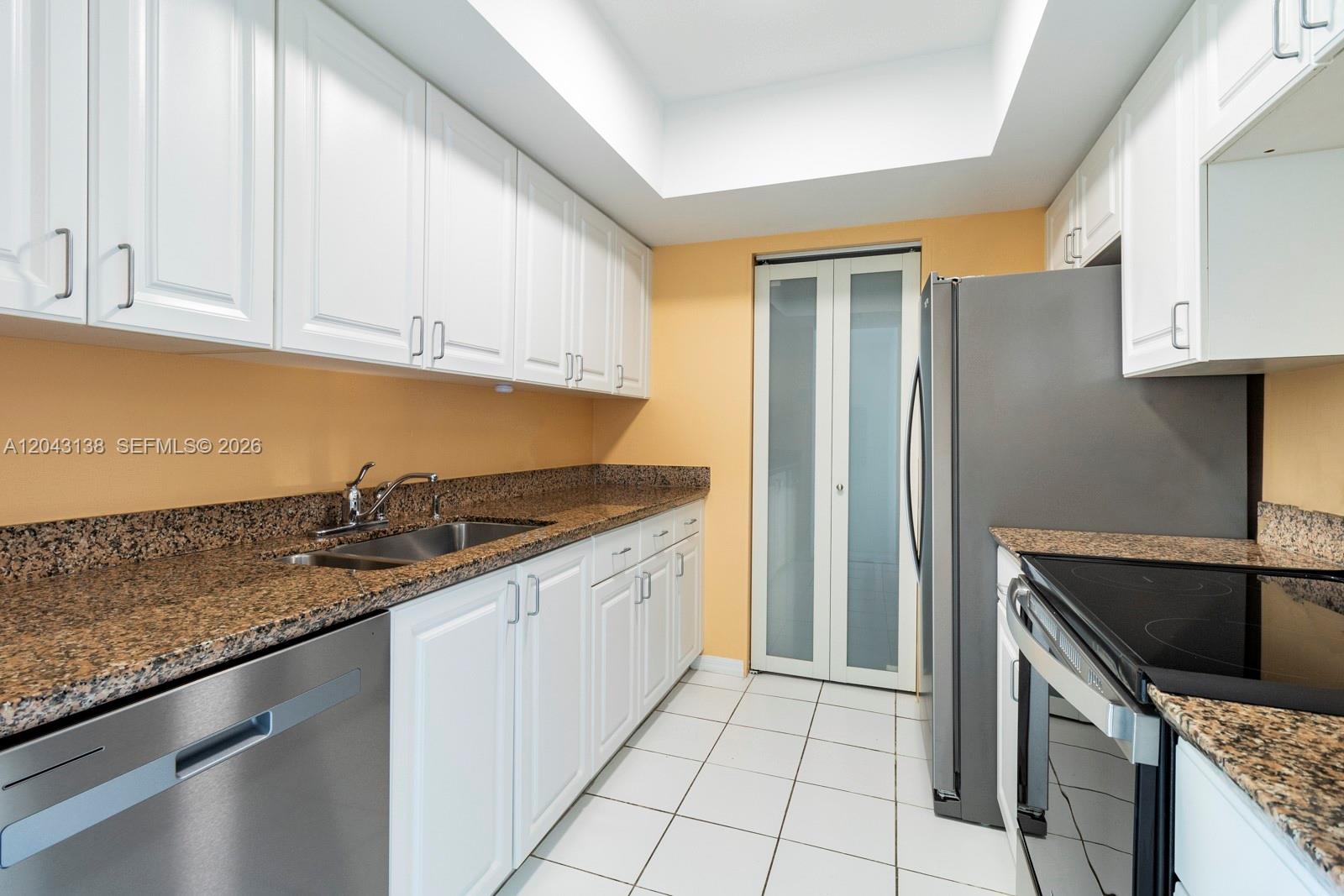 A kitchen features white cabinets, granite countertops, stainless steel appliances, and light-colored floor tiles — 90 Alton Rd # 1005, Miami Beach FL 33139, MIAMI BEACH, FL