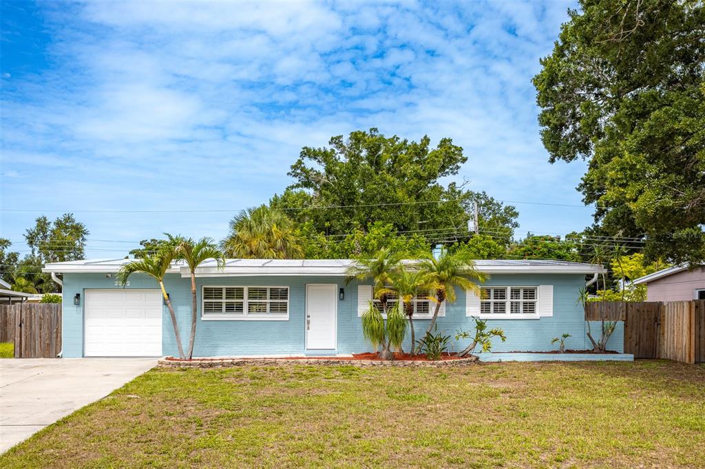 A single-story light blue house with a white garage door and palm trees in front — 3332 70TH LANE N, ST PETERSBURG, FL