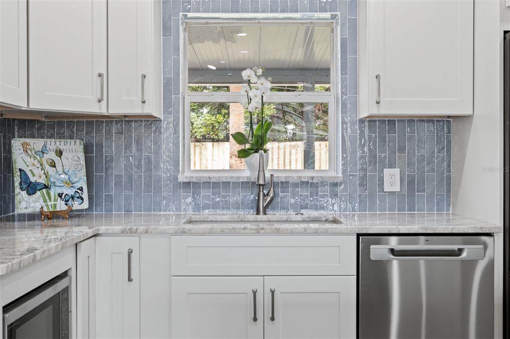A kitchen features white cabinets, a marble countertop, a blue tiled backsplash, and a sink — 3332 70TH LANE N, ST PETERSBURG, FL