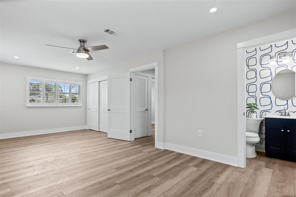 A bedroom with light wood-look flooring, a ceiling fan, and an attached bathroom with patterned wallpaper — 3332 70TH LANE N, ST PETERSBURG, FL