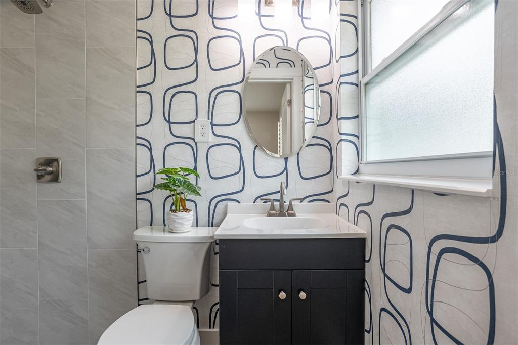 A bathroom features a dark vanity, a round mirror, and patterned wallpaper with geometric shapes — 3332 70TH LANE N, ST PETERSBURG, FL