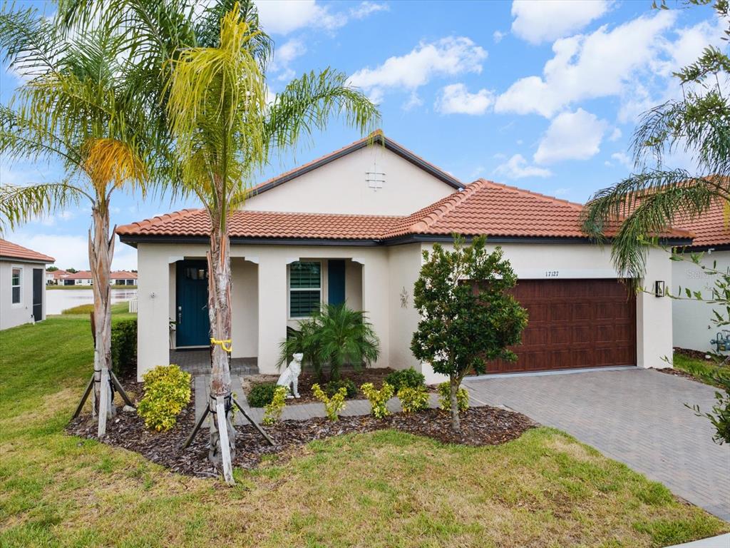 A single-story house with a tiled roof, a two-car garage, and palm trees in front — 17127 HOLLY WELL AVENUE, WIMAUMA, FL