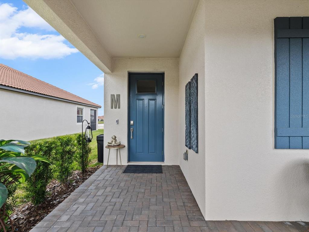 A blue front door with a small window sits under a covered porch with pavers — 17127 HOLLY WELL AVENUE, WIMAUMA, FL