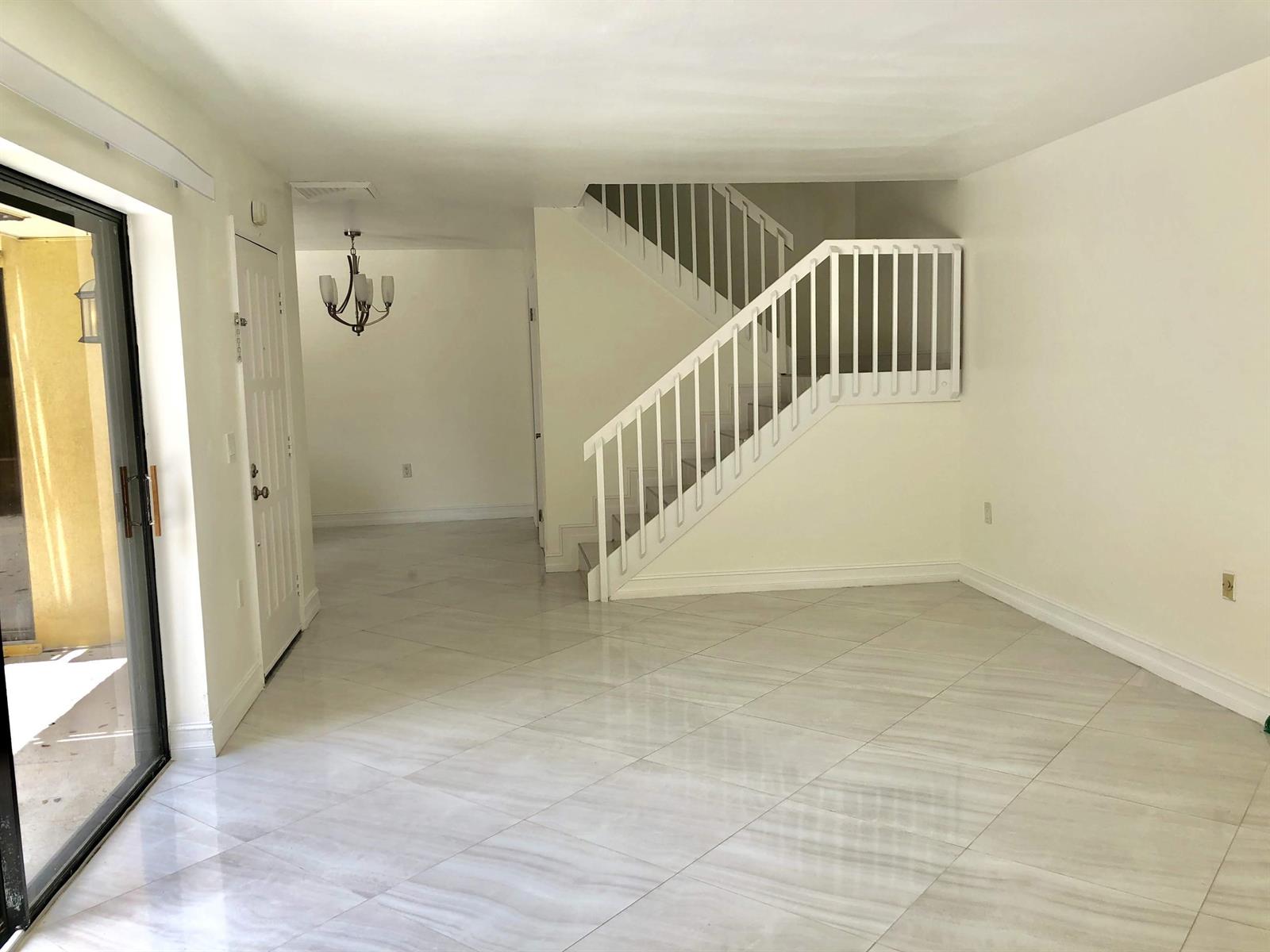An empty room with white tile floors, a staircase, and a sliding glass door — 910 9th Way, West Palm Beach FL 33407, WEST PALM BEACH, FL