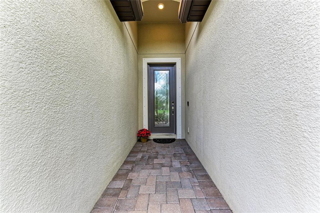 A narrow outdoor entryway features a paved walkway leading to a glass-paneled front door — 621 FIRE BUSH COURT, BRADENTON, FL
