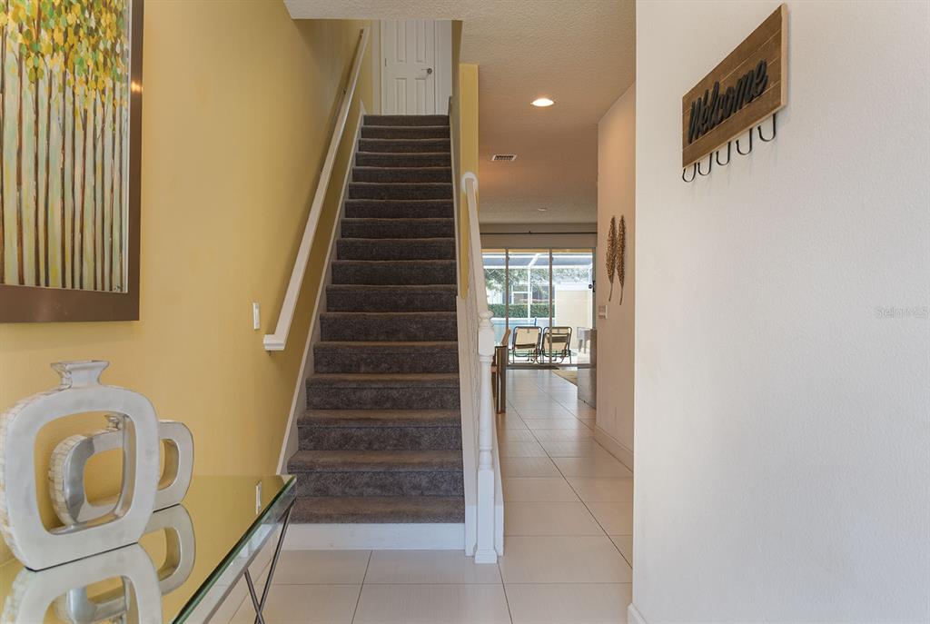 An entryway features a carpeted staircase, tile flooring, and a wall-mounted welcome sign — 1653 RETREAT CIRCLE, CLERMONT, FL